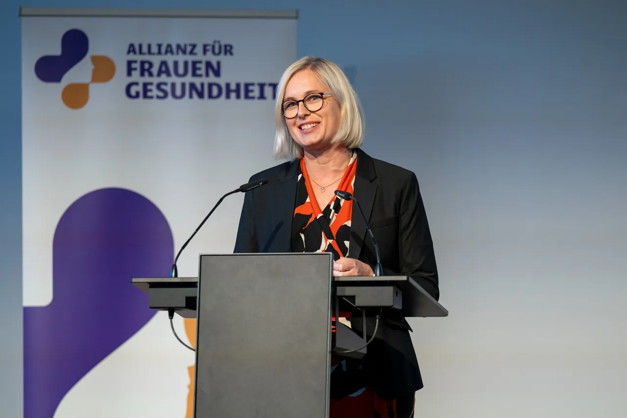 Rednerin am Pult vor dem Banner der Allianz für Frauengesundheit