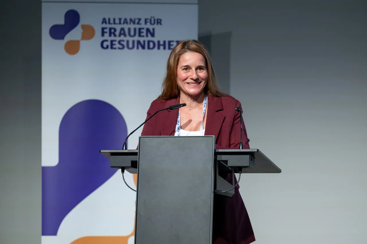 Rednerin am Pult vor dem Banner der Allianz für Frauengesundheit