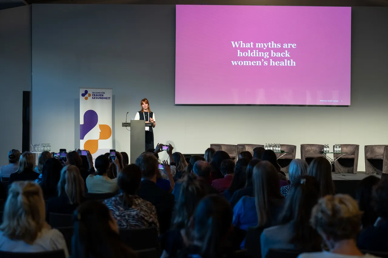 Rednerin am Pult, auf der Leinwand die Frage „What myths are holding back women’s health“